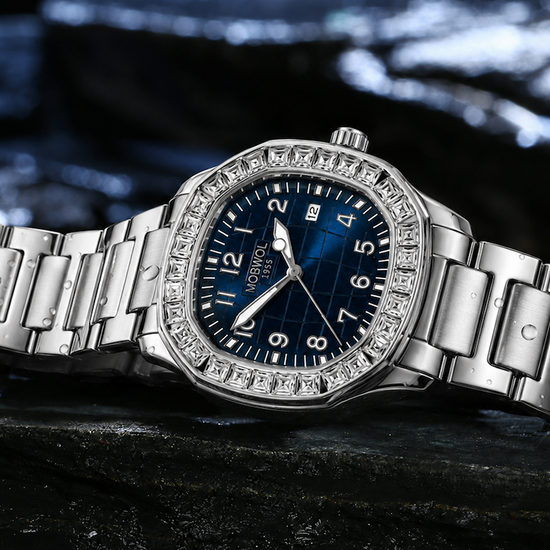 Relógio com pulseira metálica prateada, mostrador azul e bezel cravejada de pedras