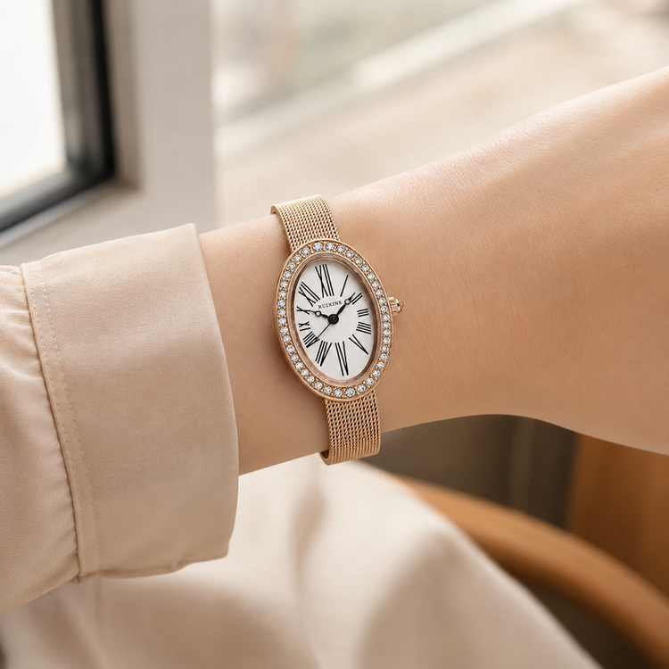 Relógio oval rosé gold no pulso, pulseira de malha metálica e mostrador branco com cristais