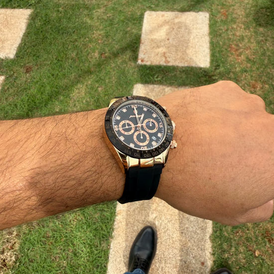 Relógio com mostrador escuro, caixa dourada e pulseira de silicone preta.