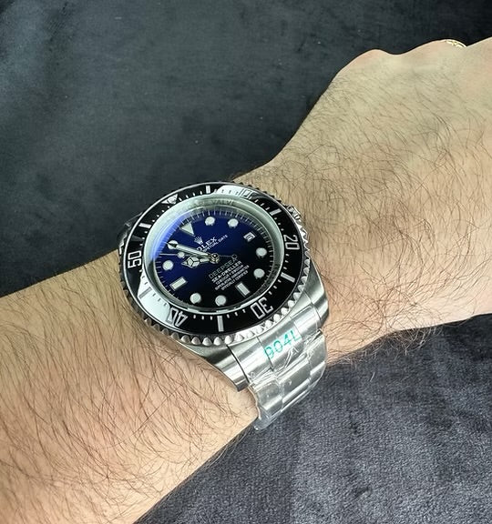 Relógio automático de aço com mostrador azul e bisel preto, no pulso.