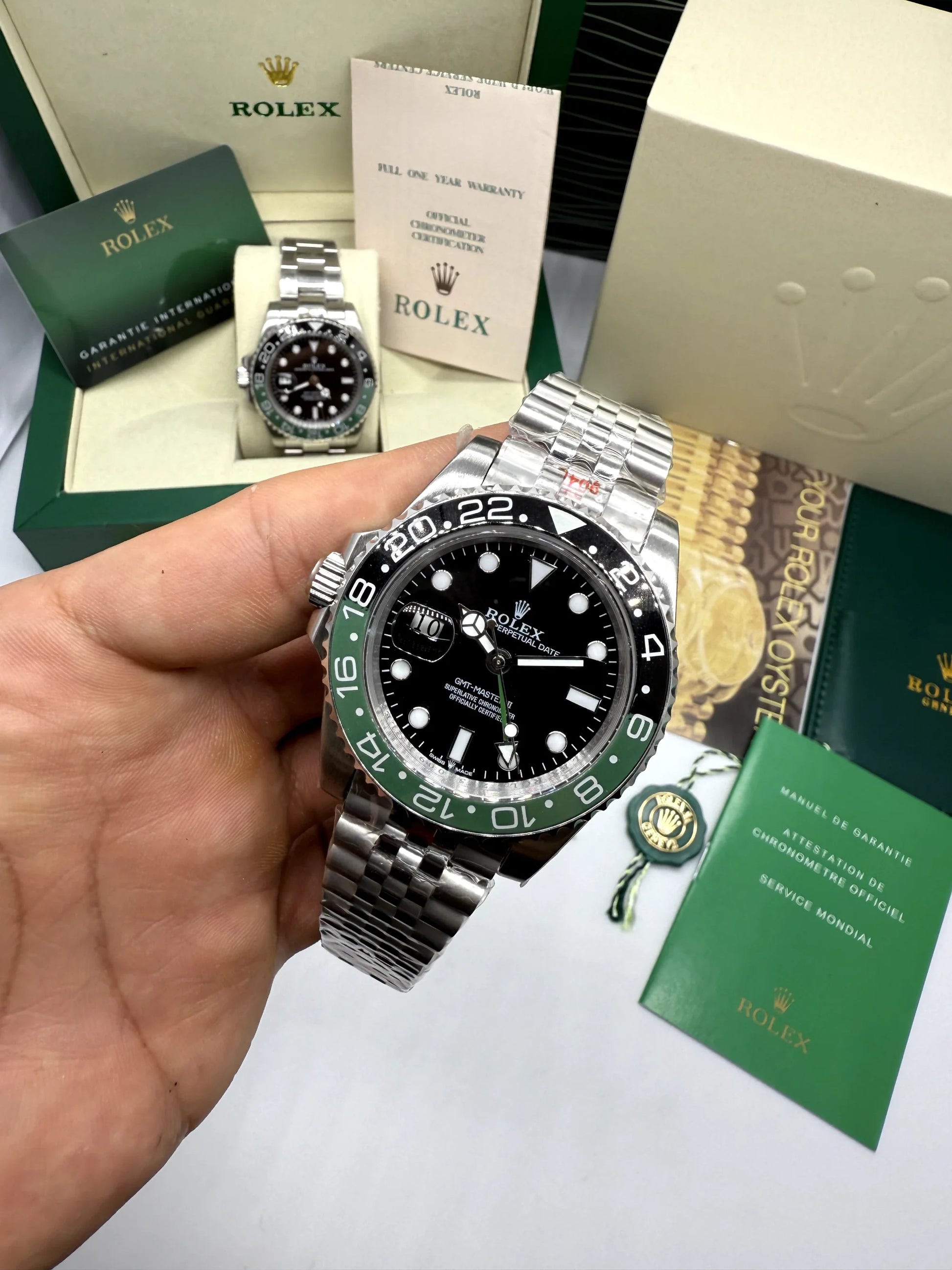 Relógio Rolex GMT Master II na mão, mostrador preto, aro verde e pulseira de aço