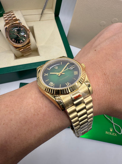Relógio Rolex dourado com mostrador verde e pulseira de aço, usado no pulso.