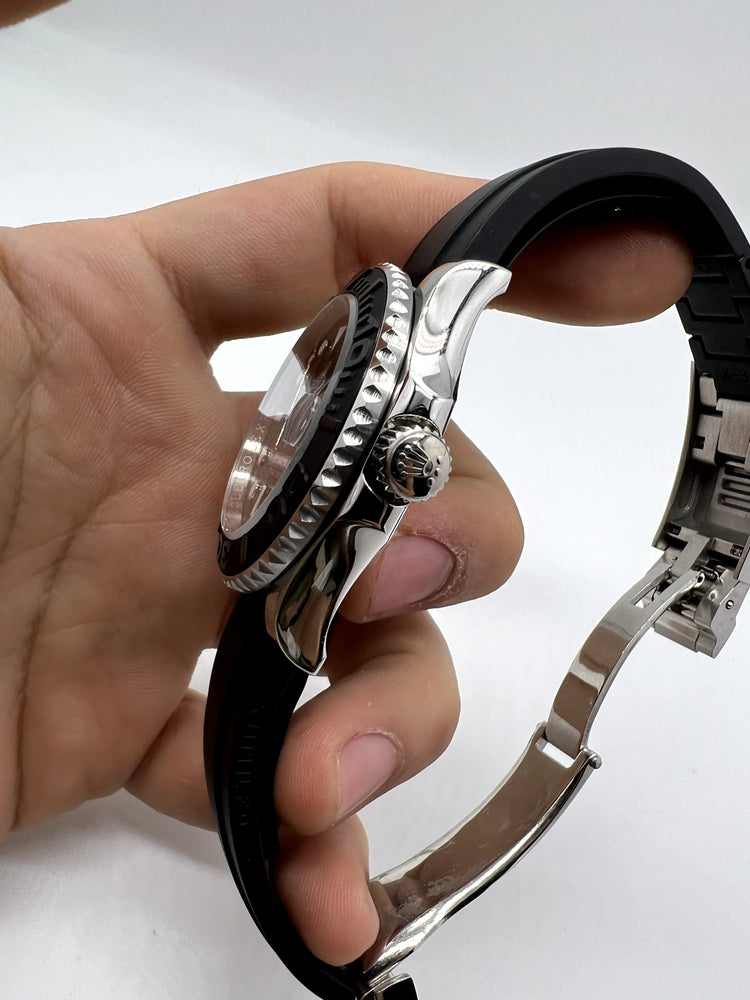 Relógio Rolex automático com caixa metálica e coroa lateral, pulseira de borracha preta.