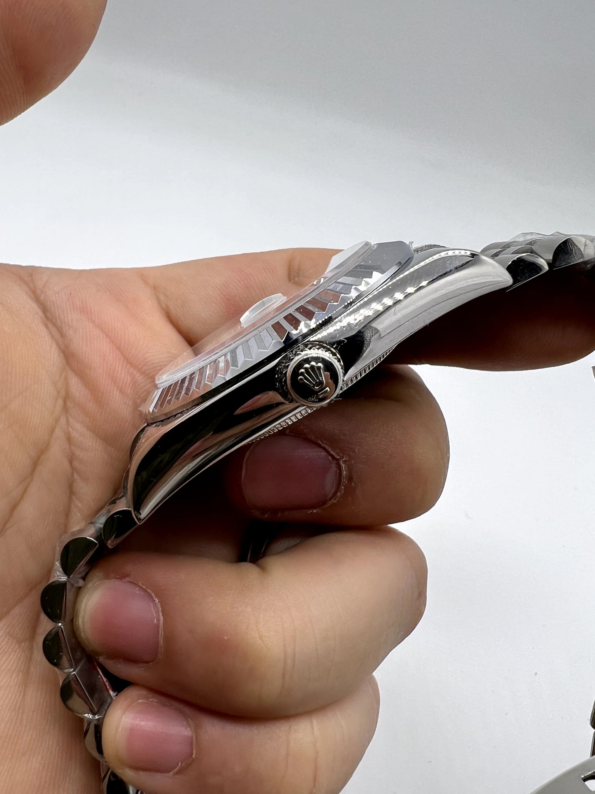 Relógio Rolex prateado de lado, com coroa e pulseira metálica, visto de perfil.