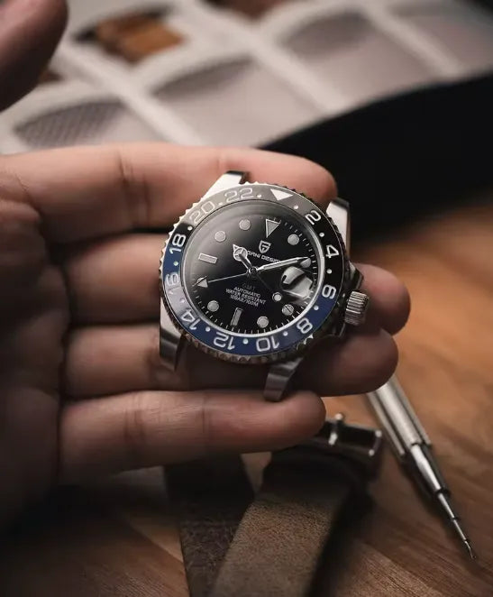 Relógio com mostrador preto e aro azul GMT, pulseira metálica, na mão