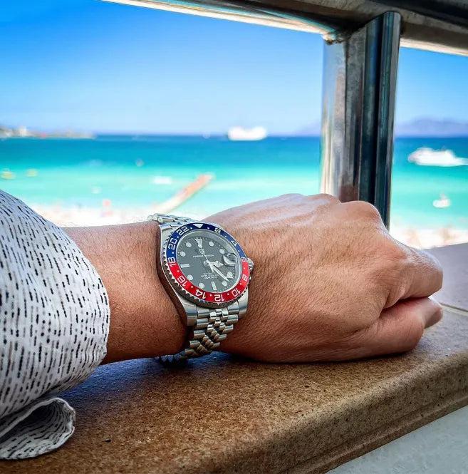 Relógio de pulso com pulseira de aço no punho, mostrador preto e bezel azul e vermelho