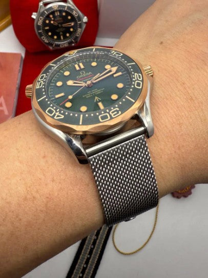 Relógio Omega na lateral, com caixa prateada e mostrador verde na pulseira mesh