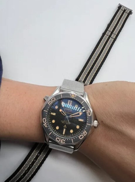 Relógio Omega no pulso, pulseira metálica e mostrador azul-escuro