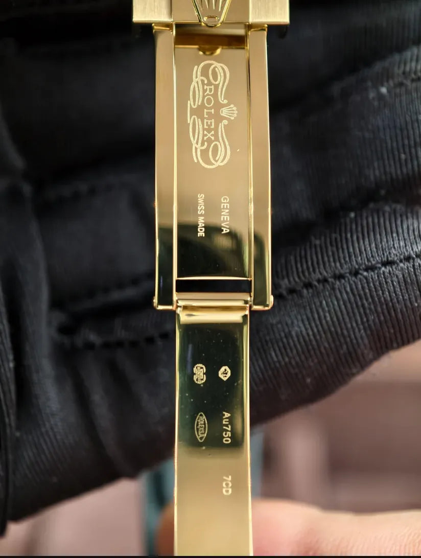 Fecho do relógio Rolex em metal dourado com gravação, sobre pulseira azul escura.