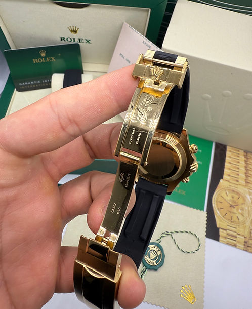 Relógio Daytona com fecho dourado e pulseira de borracha azul, parte traseira na mão.