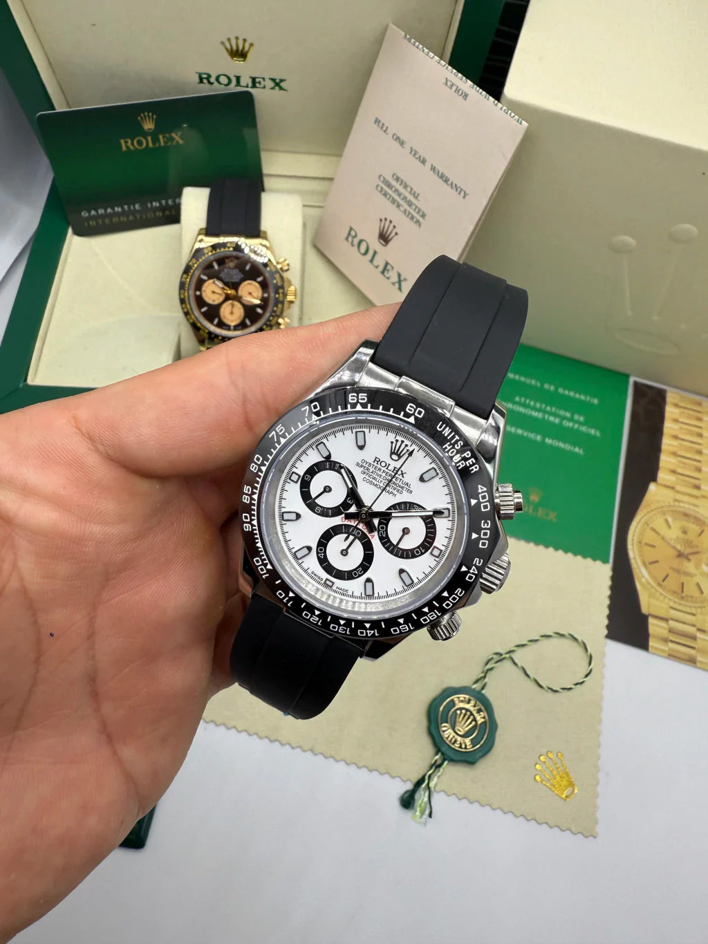 Relógio Rolex Daytona na mão, mostrado frontal branco e pulseira preta, lateral visível
