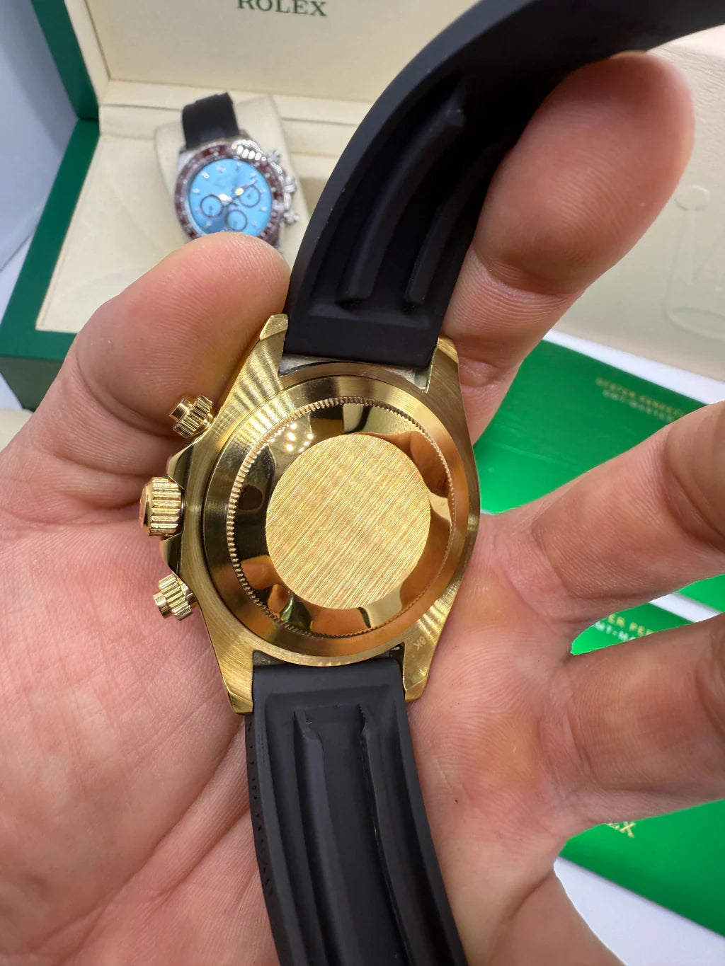 Parte traseira e laterais do relógio Rolex Daytona em ouro com pulseira azul escura.