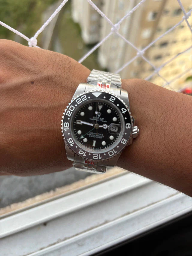 Relógio Rolex automático no pulso, mostrador preto e pulseira de aço com bezel preta