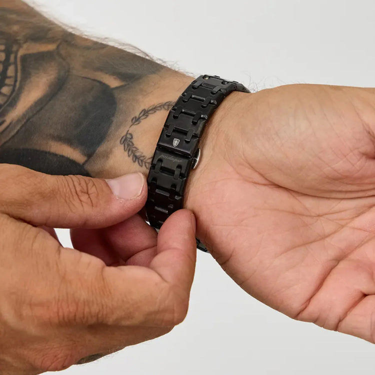Pulseira metálica escura de relógio, ajustada no pulso com fecho